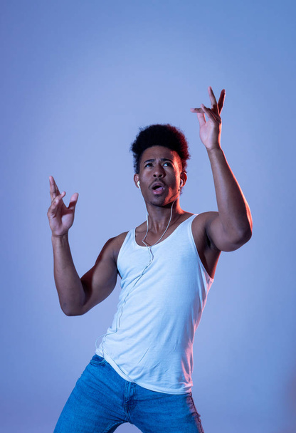 Strong african american young dancer man listening to music online dancing and singing with earphones. Artistic portrait with disco dance floor neon light in Internet Music and technology concept. - 写真・画像