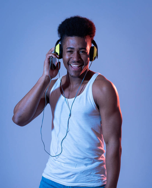 Strong african american young dancer man listening to music online dancing and singing with headphones. Artistic portrait with disco dance floor neon light in Internet Music and technology concept. - Фото, изображение