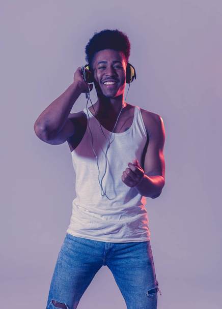 Strong african american young dancer man listening to music online dancing and singing with headphones. Artistic portrait with disco dance floor neon light in Internet Music and technology concept. - Photo, Image