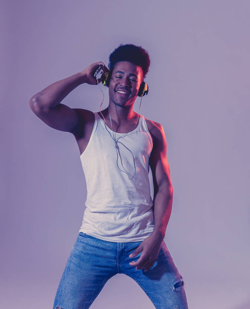 Strong african american young dancer man listening to music online dancing and singing with headphones. Artistic portrait with disco dance floor neon light in Internet Music and technology concept. - Valokuva, kuva