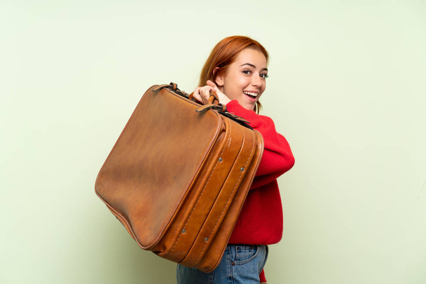 Teenager redhead girl with sweater over isolated green background holding a vintage briefcase - Fotó, kép