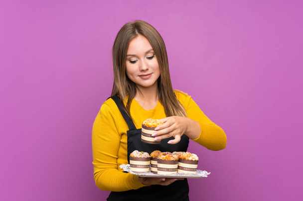 Adolescente menina segurando lotes de diferentes mini-bolos sobre isolado fundo roxo
 - Foto, Imagem