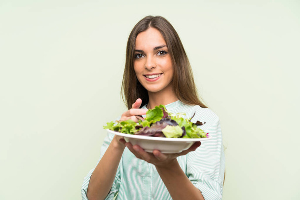 Молодая женщина с салатом над изолированной зеленой стеной
 - Фото, изображение