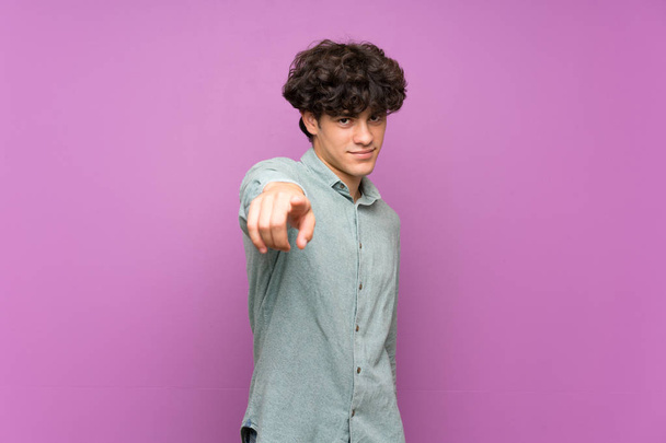 Jeune homme sur mur violet isolé pointe du doigt vers vous avec une expression confiante
 - Photo, image