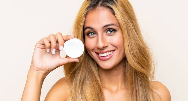Young blonde woman with moisturizer over isolated background - Photo, Image