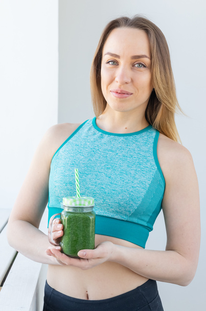 Healthy, diet, detox and weight loss concept - young woman in sportswear with green smoothie - Фото, изображение