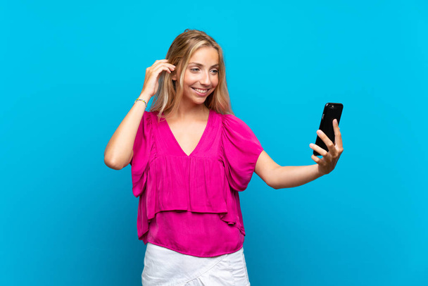 Sarışın genç kadın izole mavi arka plan üzerinde selfie yapma - Fotoğraf, Görsel