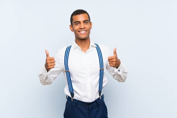 Young handsome brunette man with suspenders over isolated background giving a thumbs up gesture - Photo, Image