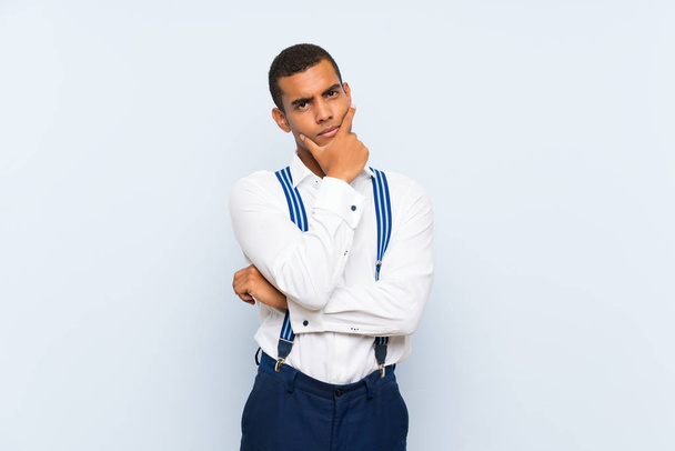 Young handsome brunette man with suspenders over isolated background thinking an idea - Photo, Image