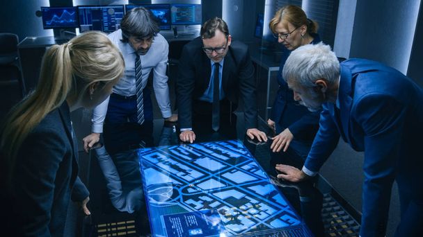 High Angle Shot of Team of Government Intelligence Agents Talking while Standing Around Digital Touch Screen Table and Tracking Suspect. Satellite Surveillance Operation in the Monitoring Room. - Fotoğraf, Görsel