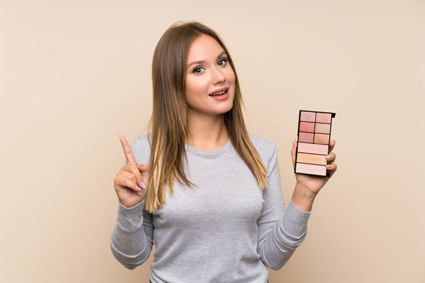 Tiener meisje met make-up palet over geïsoleerde achtergrond wijzend op een geweldig idee - Foto, afbeelding