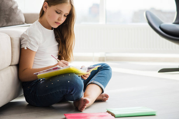 Serious school girl sit on floor write in notebook - 写真・画像