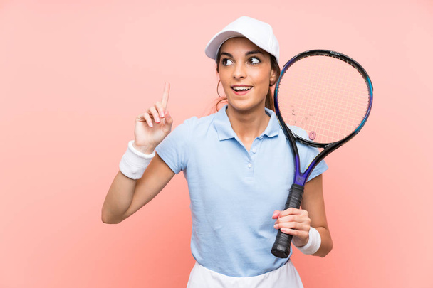 junge Tennisspielerin über isolierte rosa Wand in der Absicht, die Lösung zu realisieren, während sie einen Finger hebt - Foto, Bild