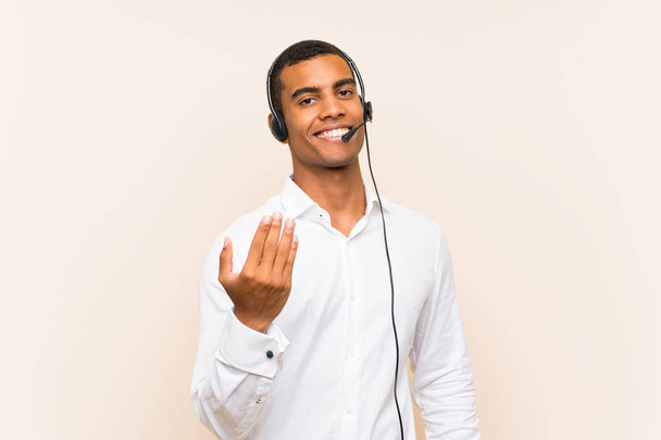 Young brunette man working with a headset inviting to come with hand. Happy that you came - Photo, Image