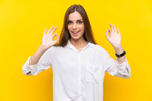 Jeune femme sur fond jaune isolé montrant un signe ok avec les doigts
 - Photo, image