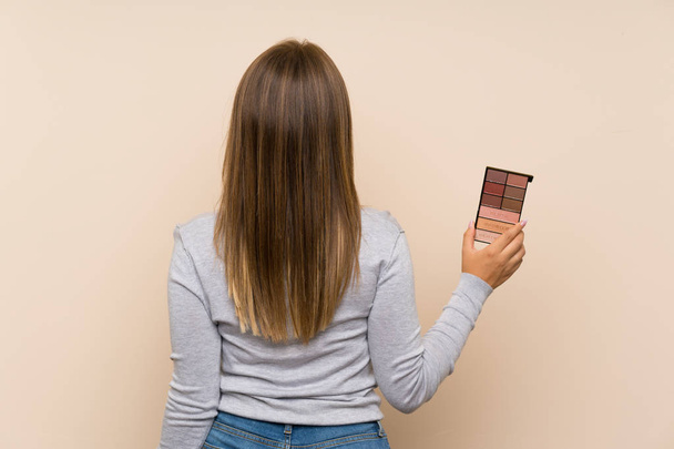 Chica adolescente con paleta de maquillaje sobre fondo aislado en la posición de la espalda
 - Foto, imagen
