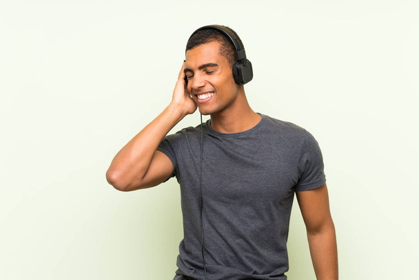 Jeune homme beau écoutant de la musique avec un mobile sur un mur vert isolé
 - Photo, image