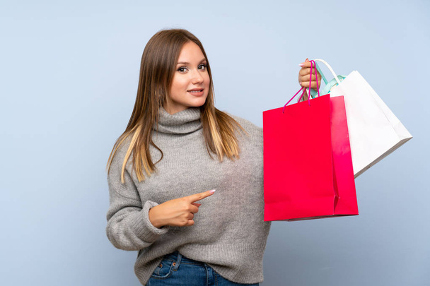 Teenager girl with sweater over isolated blue background holding a lot of shopping bags - Foto, Bild