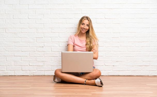 Jeune étudiante blonde avec un ordinateur portable sur le sol riant
 - Photo, image