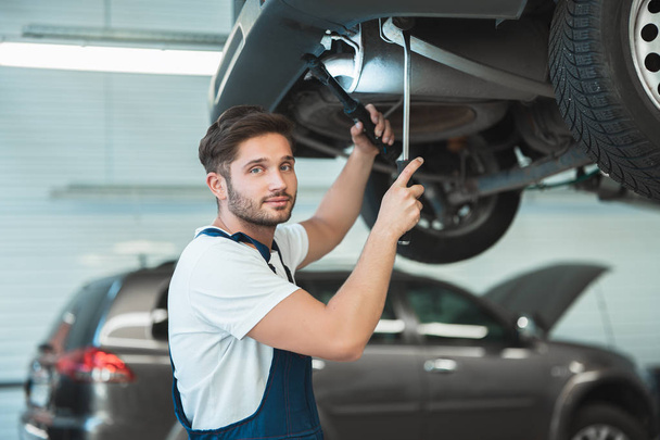 young handsome mechanic working in car service department fixing the problem in vehicle chassis - Фото, зображення