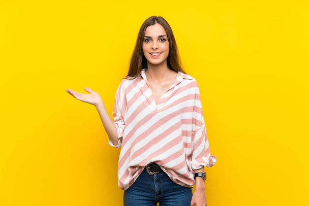 Young woman over isolated yellow background holding copyspace imaginary on the palm to insert an ad - Foto, imagen