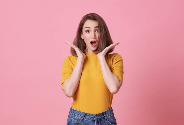 Excited beautiful woman with mouth open wearing casual yellow t-shirt isolated on pink background. - Fotó, kép