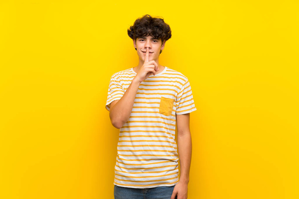 Nuori mies yli eristetty keltainen seinä osoittaa merkki hiljaisuus ele laittaa sormi suuhun
 - Valokuva, kuva