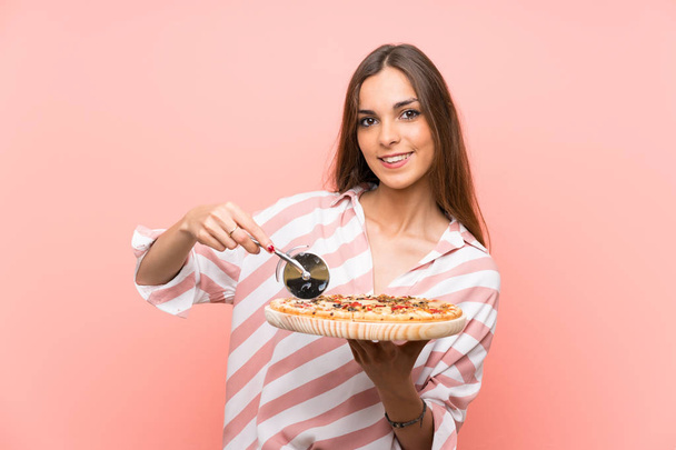 Молодая женщина держит пиццу над изолированной розовой стеной
 - Фото, изображение