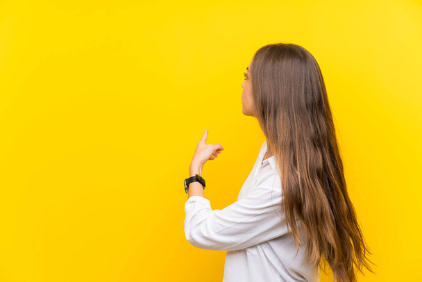 Молода жінка над ізольованим жовтим тлом, що вказує на індексний палець
 - Фото, зображення