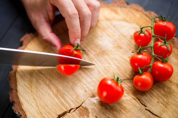 Chef slicing cherry tomatoes on a wooden board, close-up. - Фото, изображение