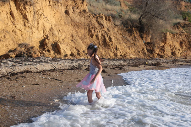 Una bambina maliziosa e allegra di otto anni con lunghi capelli castani salta sulle onde e ride con il piacere delle vacanze estive.
 - Foto, immagini