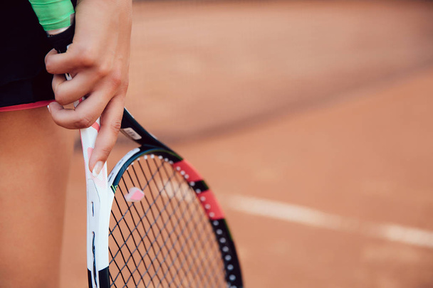 Woman holding tennis racket on clay court. Close-up view of female hand and racquet. - Photo, image