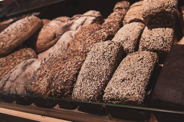 Un montón de diferentes pan saludable con semillas de girasol y sésamo en un estante de pan en una tienda de comestibles. Productos frescos de panadería de centeno
. - Foto, imagen