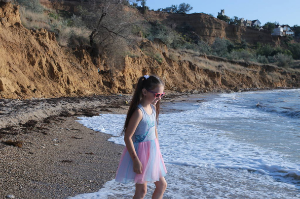 Pieni ilkikurinen ja iloinen kahdeksan vuoden tyttö, jolla on pitkät ruskeat hiukset hyppää aaltoihin ja nauraa kesälomien ilolla.
 - Valokuva, kuva