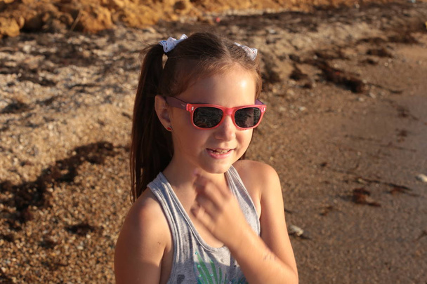 Маленькая озорная и жизнерадостная девочка восьми лет с длинными каштановыми волосами прыгает по волнам и смеется с удовольствием от летних каникул
 - Фото, изображение