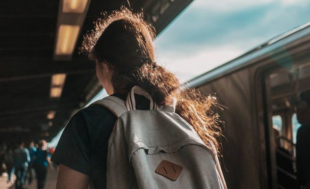 A selective focus closeup shot of a female with ponytail wearing gray backpack at a train station - Фото, зображення