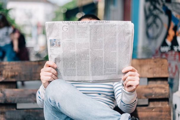 Un plano cercano de una persona sentada en un banco leyendo un periódico con un fondo borroso
 - Foto, imagen