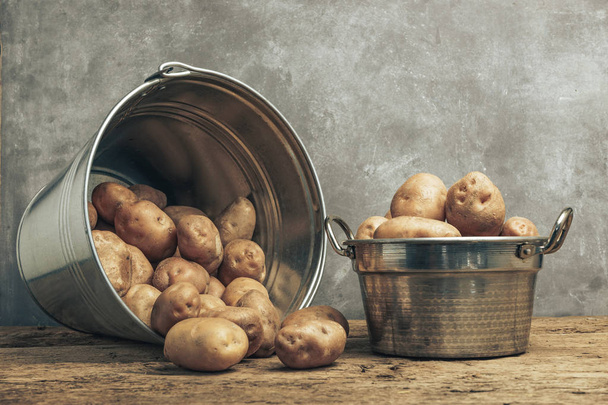 Свежий картофель в серебряной корзине на старом дубовом деревянном столе и красивом сером фоне стены
. - Фото, изображение