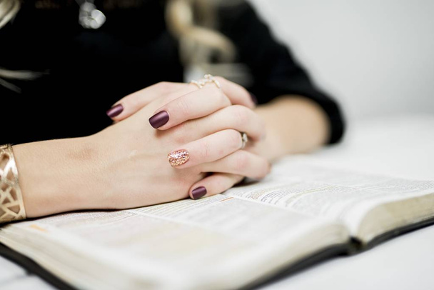 A selective focus closeup shot of a female's tightly linked fingers with rings on an open book - Фото, зображення