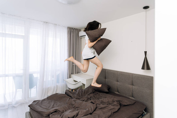Молода доросла жінка прокидається і стрибає на ліжку
 - Фото, зображення