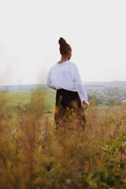 A vertical shot of a beautiful African-American female standing in a beautiful field under a clear sky - Φωτογραφία, εικόνα