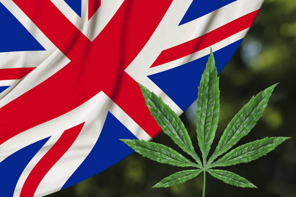 green leaf of hemp and the beautiful silk national flag of great britain, concept of medical cannabis, legalization of drugs, crime of drug dealers, close-up - Fotó, kép