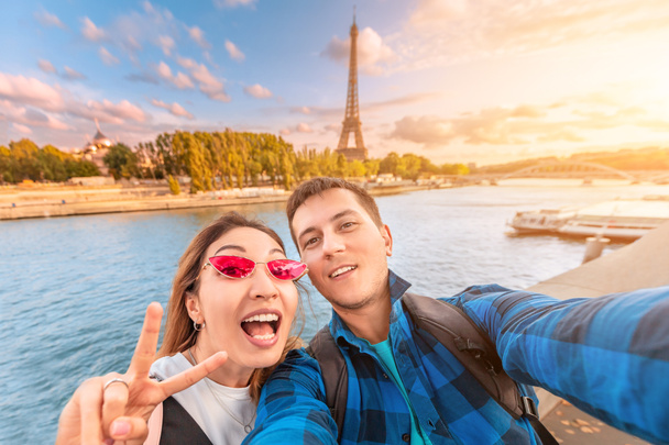 愛の幸せなカップルは、男と女性が抱き合い、背景にエッフェル塔とセーヌ川のほとりで自分撮りを取ります。パリとフランスの旅行と休暇 - 写真・画像