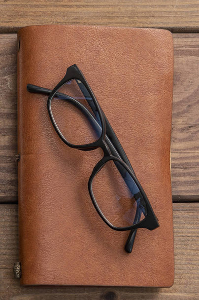 old glasses with vintage style notebook on wooden background - Fotó, kép