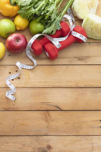 fresh organic vegetables, dumbbells and tape measure on wooden background - Photo, Image