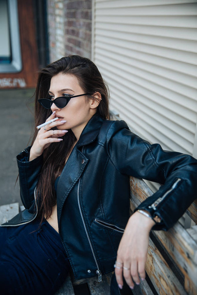 young girl in a leather jacket smokes cigarettes, rock style, cheeky and cute girl street posing style, rock punk lifestyle - Fotoğraf, Görsel