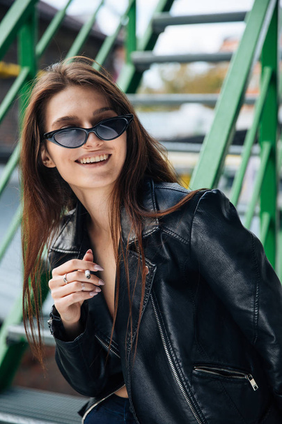 young girl in a leather jacket smokes cigarettes, rock style, cheeky and cute girl street posing style, rock punk lifestyle - Photo, image