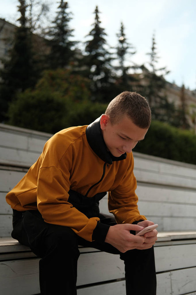 κομψό περιστασιακό έφηβο αγόρι σε μοντέρνο κίτρινο και μαύρο σμόκιν σακάκι χρησιμοποιώντας το κινητό τηλέφωνο - Φωτογραφία, εικόνα