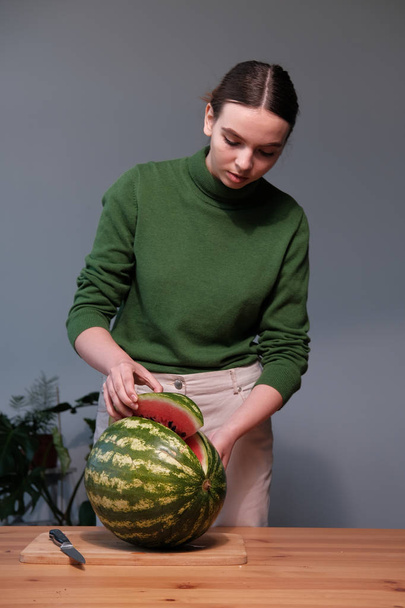 young woman cutting watermelon in home interior - Фото, изображение