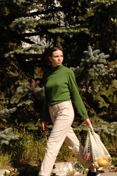 Nuori nainen vihreässä villapaita kävely laukku päivittäistavarat kadulla ulkoa
 - Valokuva, kuva
